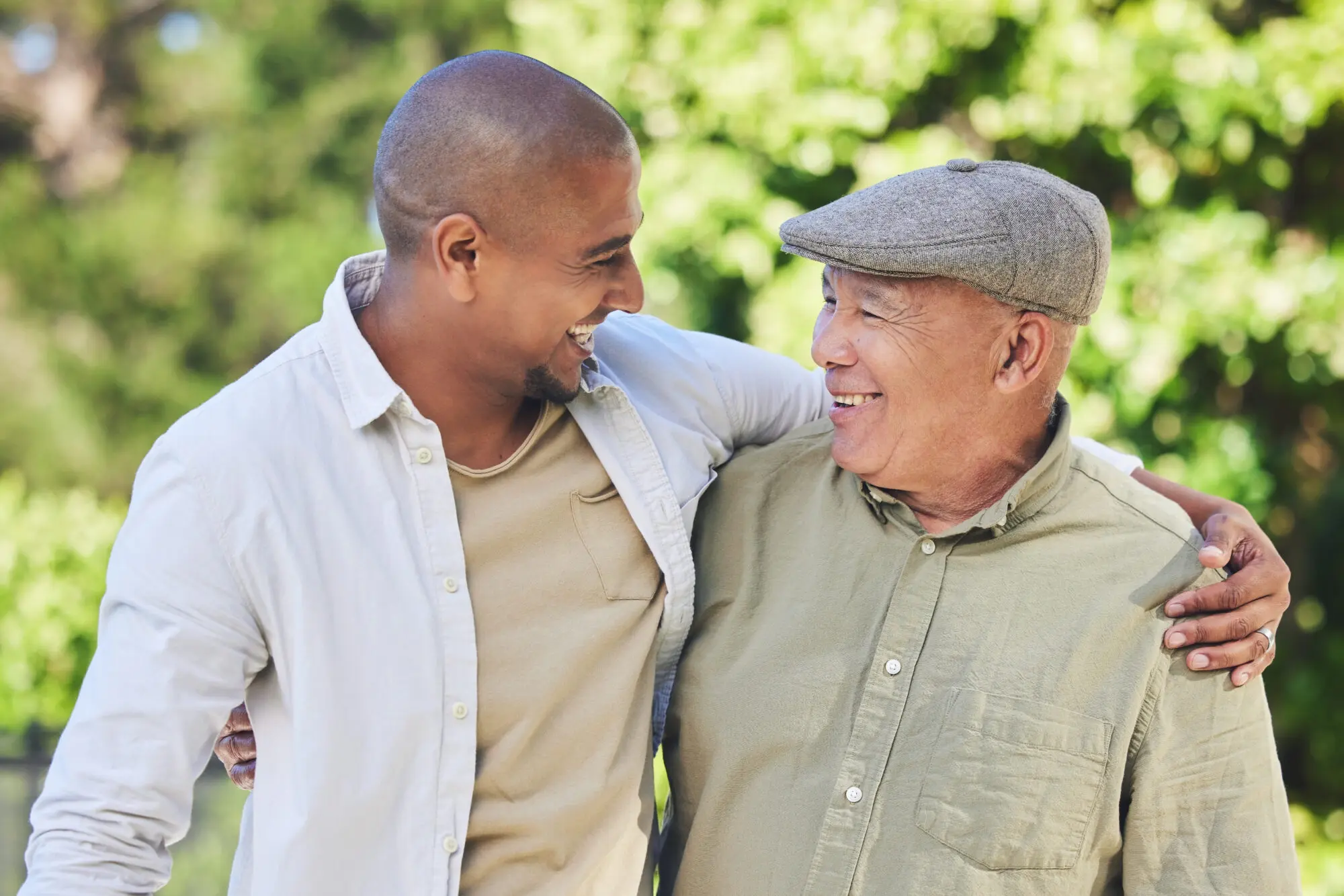 Older father and adult son smiling with their arms around each other outdoors